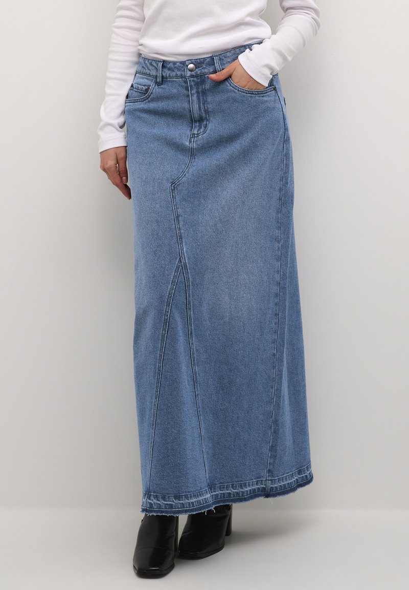 Light blue denim maxi skirt with a straight cut, front pocket, and sewn knee panel seams. Worn with black heeled boots.