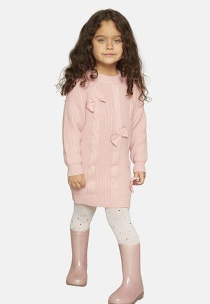 Abito rosa a maglia con design a treccia, fiocchi e polsini a coste. Indossato sopra leggings bianchi a pois e stivaletti da pioggia rosa lucidi.