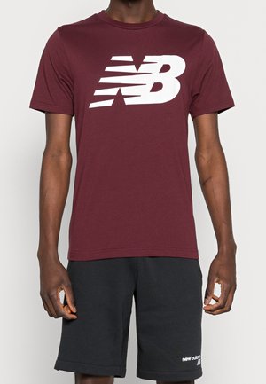 Burgundy short-sleeve T-shirt in soft fabric features a large white "NB" logo. Paired with black shorts, detailing along the hem is visible.
