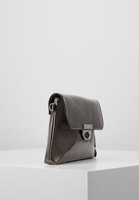 Lædertaske i mørkt metallisk grå med en struktureret form, fold-over klap, sølvhardware og en dekorativ lås.