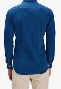 Camicia in denim blu con maniche lunghe, polsini allacciati, orlo curvo e dettagli della cucitura del giromanica sul retro. Tessuto morbido e design del colletto classico.