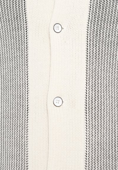 Knit cardigan featuring a cream and black striped pattern, two buttons, with a textured fabric. The design has a structured, cozy appearance.