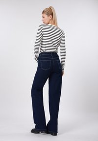 Φαρδιά μπλε τζιν με ψηλή μέση, σε συνδυασμό με μακρυμάνικη μπλούζα σε ασπρόμαυρες ρίγες. Διαθέτει βασικό ντεκολτέ και τσέπες στο πίσω μέρος.