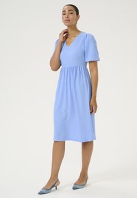 Ljusblå, kortärmad klänning med V-ringning och rynkad midja. Tillverkad av textil med struktur, knälång, kompletterad med blå slingback-klackar.