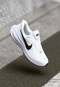 Baskets blanches à enfiler avec dessus en mesh texturé, logo Nike noir, et semelle intermédiaire blanche. Forme arrondie avec semelle extérieure noire pour une meilleure adhérence.