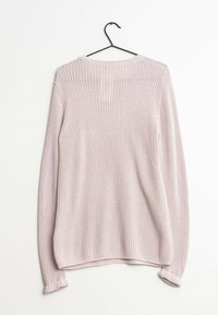 Ljust rosa stickad tröja med långa ärmar hängande på en svart galge mot en vit bakgrund.