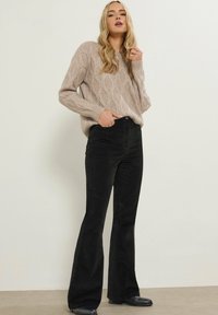 Beige kabelgebreide trui met een relaxte pasvorm, gecombineerd met hoge zwarte flared corduroy broek. Getextureerde stof en subtiele details.