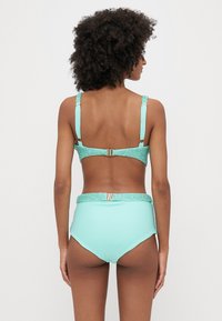 Ένα δι-part μαγιό σε απόχρωση μέντας, με υφασμάτινες γκλίτερ τιράντες και λεπτομέρειες στη μέση, και σχέδιο ψηλόμεσου σλιπ.