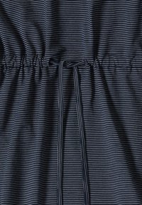 Gros plan d’un tissu foncé à fines rayures blanches horizontales et d’une taille froncée attachée avec des cordons en tissu rayé assorti.