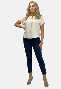 Jasnoróżowa bluzka z krótkim rękawem o fasonie z plisami, zestawiona z granatowymi spodniami wąskimi. Całość uzupełniają wzorzyste szpilki.