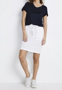 Marinblå kortärmad topp i kombination med en vit snörskjorta, som framhäver en slät textur. Bärs med vita sneakers för en avslappnad look.