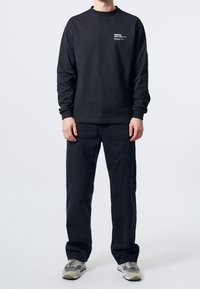 Černá mikina s kulatým výstřihem a dlouhými rukávy, spárovaná s odpovídajícími černými kalhotami. Obsahuje bílé grafické logo na hrudi. Šedé tenisky.