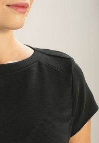 Top nero texturizzato con scollo rotondo e maniche corte. Presenta cuciture e dettagli di cucitura sottili sulla spalla.