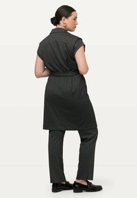Grau gestreifter Anzug mit einem ärmellosen Blazer und passenden schmalen Hosen. Verfügt über eine taillierte Taille und schwarze Slipper. Minimalistisches Design.