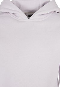 Sudadera gris claro con una textura suave y lisa. Cuenta con una capucha con doble forro y una etiqueta central en el cuello. Sin patrones ni piezas visibles.