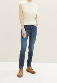 Světlý krémový bezrukávový top s texturou spárovaný s úzkými tmavě modrými džíny a světlými šněrovacími kotníkovými lahvemi. Jednoduchý a moderní design.