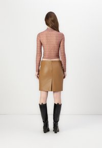 Langermet, rosa gjennomsiktig topp med gjentakende logo mønster, paret med et høydeintelligent, brunt skinnskjørt med en bakslitz og svarte hælboots.