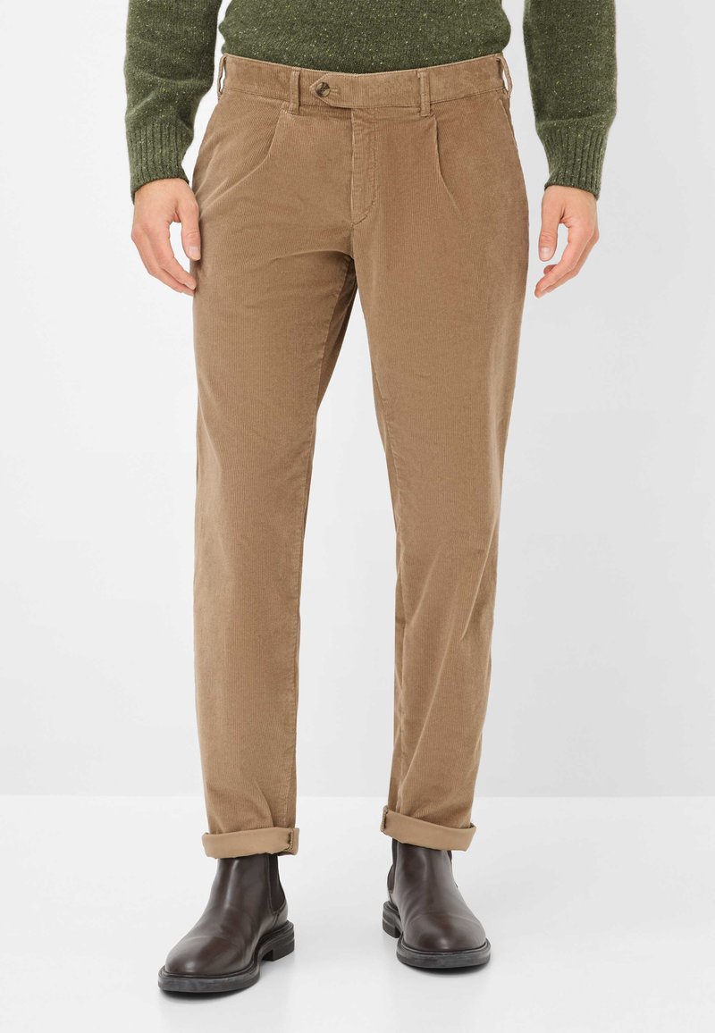 Pantaloni in corda marrone con gamba dritta, dotati di chiusura con bottone, pieghe frontali e orli arrotolati, abbinati a stivaletti neri alla caviglia.