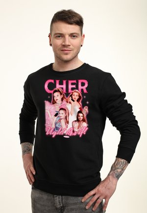 Mand iført sort sweatshirt med pink "CHER" tekst og billeder af fire kvinder fra filmen "Clueless" med sloganet "Ugh! As if!".