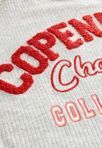 Grauer gerippter Sweatshirt mit roher strukturierter Stickerei, die "KOPENHAGEN" und "COLLEGE" buchstabiert, sowie zusätzlichen roten geschwungenen Akzenten.