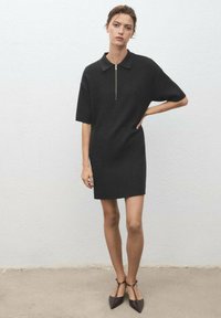 Black knit dress with a polo collar, short sleeves, and a central zipper. Fitted shape, smooth texture, and knee-length design.