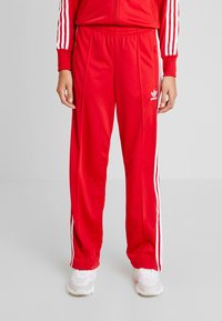 Röda polyester träningsoverallsbyxor med vita sidostreifen och elastisk midja. Har en sportig silhuett och broderad logotypdetalj.