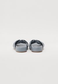 Sandales gris en plastique avec un design à lanière tressée, texture lisse et semelle épaisse. La semelle inférieure est plate et légèrement texturée.