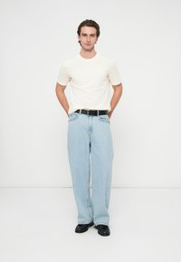 Krótki kremowy t-shirt z krótkim rękawem w połączeniu z luźnymi jasnoniebieskimi dżinsami o prostych nogawkach i czarnym paskiem.