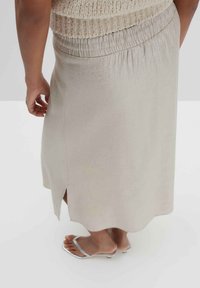 Helles beigefarbenes Midikleid mit elastischem Bund und seitlichem Schlitz. Hergestellt aus glattem Stoff mit leichtem Glanz. Kombiniert mit silbernen Flip-Flops.