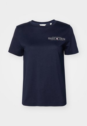 Camiseta de algodón azul marino de mangas cortas, con cuello redondo y un logo impreso que presenta "GANT 1949" en el lado izquierdo del pecho. Textura suave.