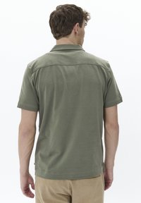Polo de manga corta en verde oliva con cuello, textura suave y dobladillo recto. Costuras visibles en los hombros y los lados.