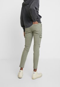 Olivgröna cargobyxor med sidofickor, smal passform och något avsmalnande ben. Kombineras med en grå hoodie och beige höga sneakers.