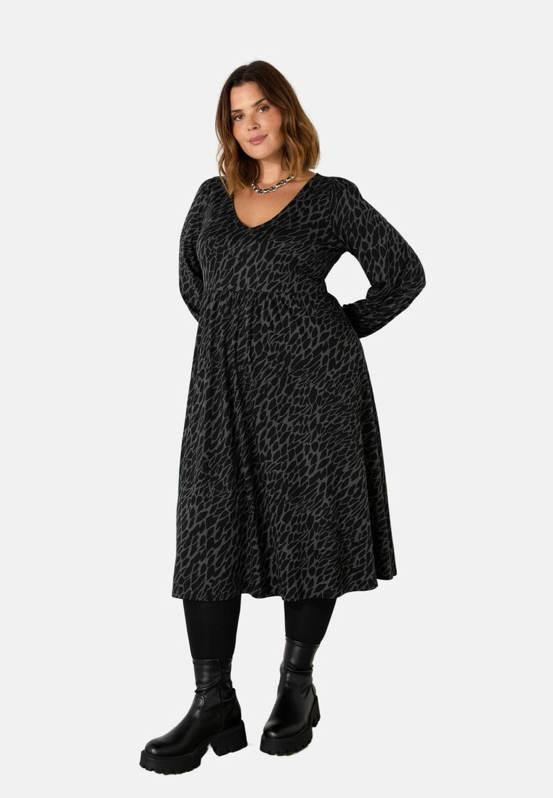 Musta mekko, jossa on leopardikuosi, V-mallinen pääntie, pitkät hihat ja leveähelma, yhdistettynä mustiin nilkkureihin.