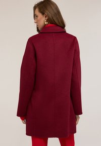 Cappotto in lana color bordeaux con colletto classico, vestibilità su misura, maniche lunghe e una texture liscia, caratterizzato da una silhouette pulita e senza motivi visibili.