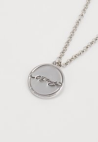 Silver chain necklace featuring a circular pendant with a glossy gray surface and embossed signature detail. Simple and modern design.