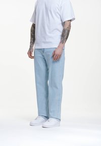Světle modré džíny s volným střihem, kombinované s jednoduchým bílým tričkem a bílými teniskami, představují neformální outfit.