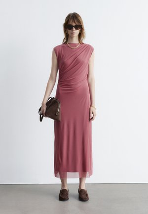 Mauve ärmelloses Kleid mit drapierten Details, knielanger Saum, kombiniert mit einer braunen Handtasche und Slippern, getragen mit Sonnenbrille.