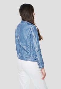 Spijkerjack met een lichtblauwe wassing, voorzien van gestikte accenten, zijritsdetails en een aansluitend ontwerp. Gezien van achteren, gecombineerd met witte broek.