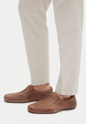 Brązowe skórzane buty wsuwane z przeszyciami, teksturowaną powierzchnią i elastyczną podeszwą, w połączeniu z jasnymi spodniami.