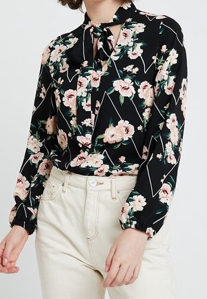 Blusa nera a maniche lunghe con stampa floreale in rosa e verde, con colletto annodato e accenti geometrici bianchi. Tessuto morbido con vestibilità ampia.