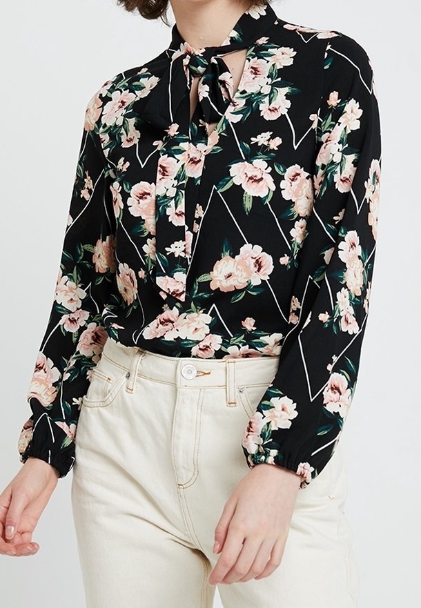 Blusa nera a maniche lunghe con stampa floreale in rosa e verde, con colletto annodato e accenti geometrici bianchi. Tessuto morbido con vestibilità ampia.