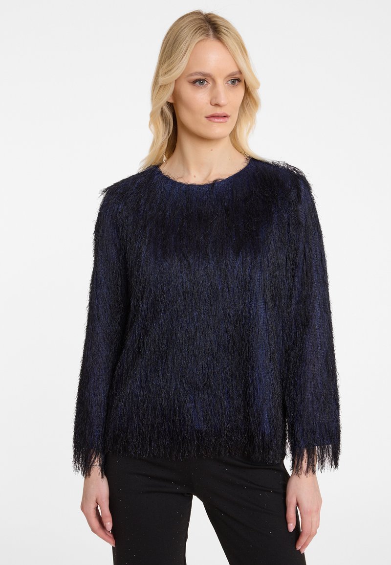 Dunkelblauer, flauschiger Pullover mit langen Ärmeln und rundem Halsausschnitt. Das Material hat ein strukturiertes, fransiges Aussehen. Kombiniert mit schwarzen Hosen.