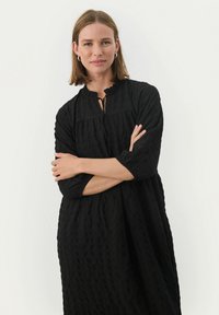 Schwarzes strukturiertes Kleid mit Rundhalsausschnitt, Rüschensaum und drei Viertelärmeln, das eine lässige Passform und dezente Falten aufweist.