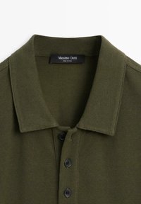 Polo vert olive avec trois boutons noirs et un col ouvert, étiquette Massimo Dutti, fabriqué en Chine.