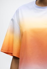 Μπλούζα με κοντά μανίκια και στρογγυλή λαιμόκοψη με ομαλή απόχρωση από λευκό στο πάνω μέρος σε πορτοκαλί και ροδακινί τόνους στο κάτω μέρος.