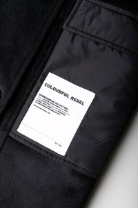 Casaco preto com um rótulo retangular branco a dizer "Colourful Rebel" e detalhes sobre uma coleção de roupas femininas cosidos no forro.