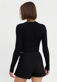 Débardeur noir côtelé à manches longues et à coupe ajustée, associé à un short noir taille haute avec deux poches arrière.