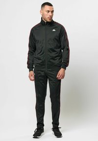 Zwarte sportieve trainingsoutfit van gladde stof; heeft rode zijstrepen en een hoge kraag, met elastische manchetten en tailleband.