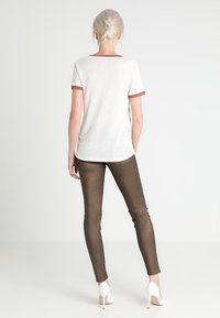 Camiseta blanca con cuello y mangas de canalé rojos, combinada con leggings marrones brillantes. El conjunto se completa con tacones altos blancos.