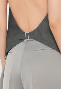 Halli denim ülaosa avatud seljaga, kus on lihtne hõbedane detail vööl. Koos heledast hallist kohandatud pükstega.